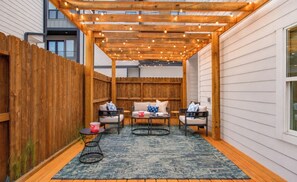 A covered patio area with a wooden pergola, outdoor seating, and a view of a building. - Spa Soaker Tub & Patio Near Downtown Houston & University of Houston (Houston)