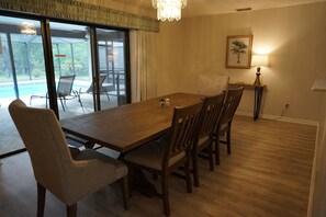 A dining area with a wooden table and chairs, a lamp, and a view of a pool through glass doors. - Rainbow springs oasis with solar heated pool. (Dunnellon)