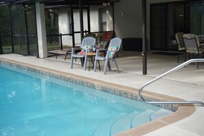 A pool area with a table and chairs, a covered seating area, and a glass-enclosed space. - Rainbow springs oasis with solar heated pool. (Dunnellon)