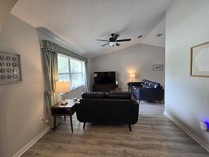 Un salon avec un ventilateur de plafond, un téléviseur, un canapé et une lampe.