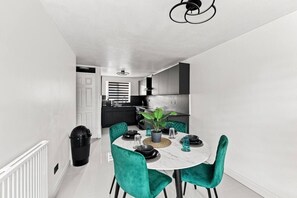 Een moderne keuken met zwarte kasten, roestvrijstalen apparatuur en een eethoek met een ronde tafel en teal stoelen.