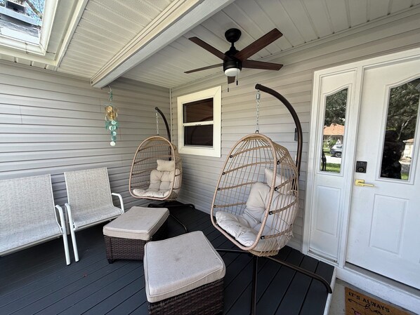 A porch with two wicker chairs, a bench, and a ceiling fan.