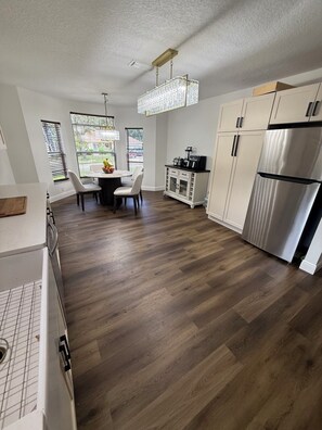 A modern kitchen with a dining area, wooden flooring, and a stainless steel refrigerator.