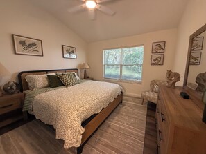 A bedroom with a bed, nightstands, a lamp, a window with blinds, and wall art.