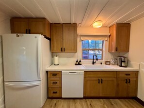 Una cocina con armarios de madera, un refrigerador blanco, un lavavajillas, una ventana con vistas y una cafetera.