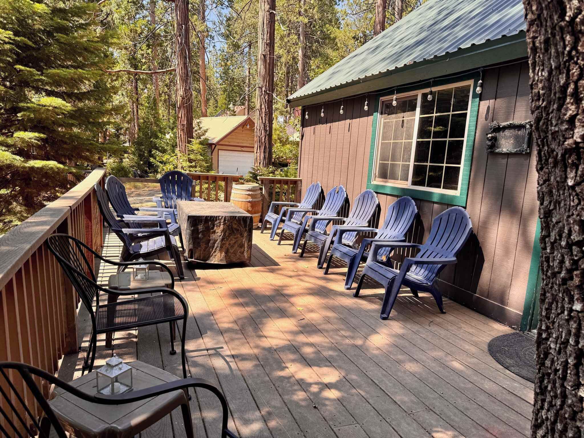 A wooden deck with outdoor seating, including chairs and tables, surrounded by trees.