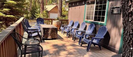 A wooden deck with outdoor seating, including chairs and tables, surrounded by trees.