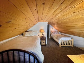 A small, attic-style bedroom with two single beds, a nightstand with a lamp, and a wooden ceiling. - Foxtail Cabin - Walk to Town & West Village (Shaver Lake)