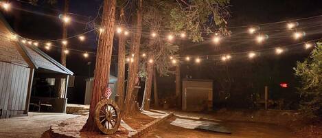 A rustic outdoor setting with a dirt path, wooden structures, and string lights.