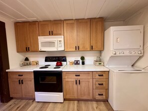 A kitchen with wooden cabinets, a microwave, a stove, and a refrigerator. - Foxtail Cabin - Walk to Town & West Village (Shaver Lake)