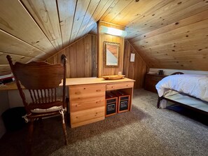 Un dormitorio acogedor en el ático con un escritorio de madera, una silla, una cama y un aparador.