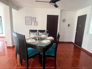 A dining area with a round table set for four, black chairs with teal cushions, and framed wall art above the table.