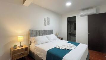 Una camera da letto con un letto, comodini, una lampada, un condizionatore d'aria a parete e una porta.