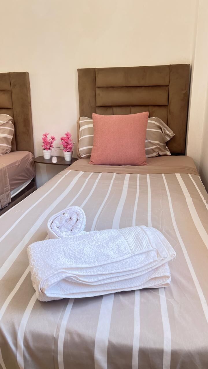 A neatly made bed with striped bedding, a folded white towel, and a pink pillow.