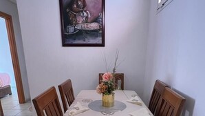 Zona pranzo con tavolo apparecchiato per quattro, circondato da sedie di legno, un quadro appeso al muro e un vaso con fiori sul tavolo.