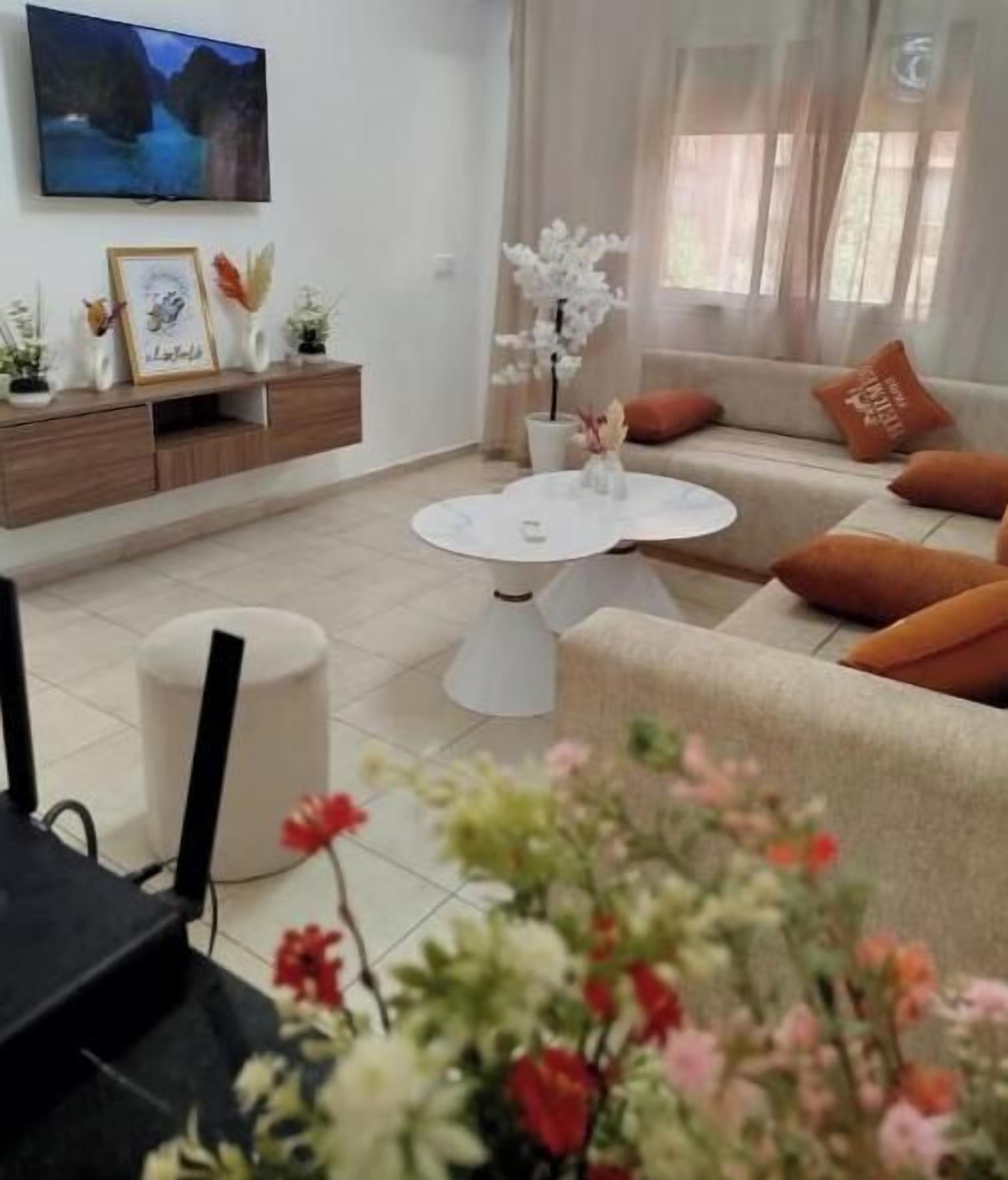 A living room with a sofa, a coffee table, a TV mounted on the wall, and a cabinet with decorative items.