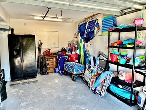 Een rommelige garage met een koelkast, planken vol spullen en een prikbord aan de muur.