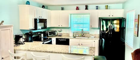 A kitchen with white cabinets, a black refrigerator, a granite countertop, and a window with blinds.