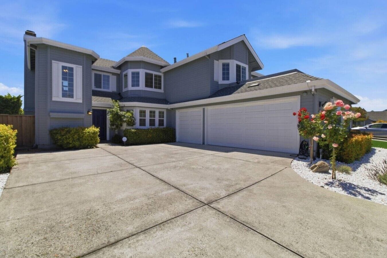 A two-story house with a garage, a driveway, and a small garden with flowers.