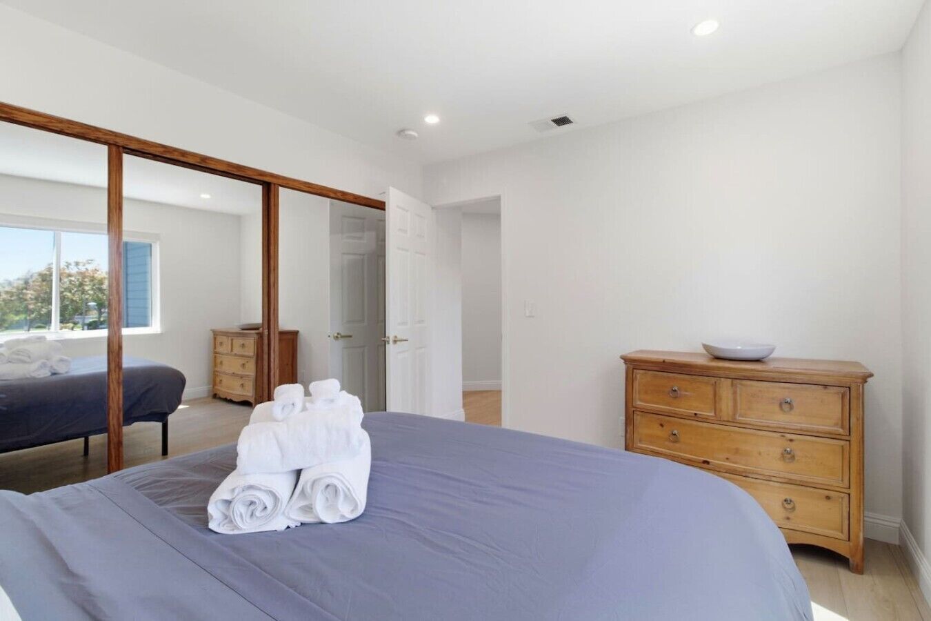 A bedroom with a bed, a wooden dresser, and a sliding door leading to another room.