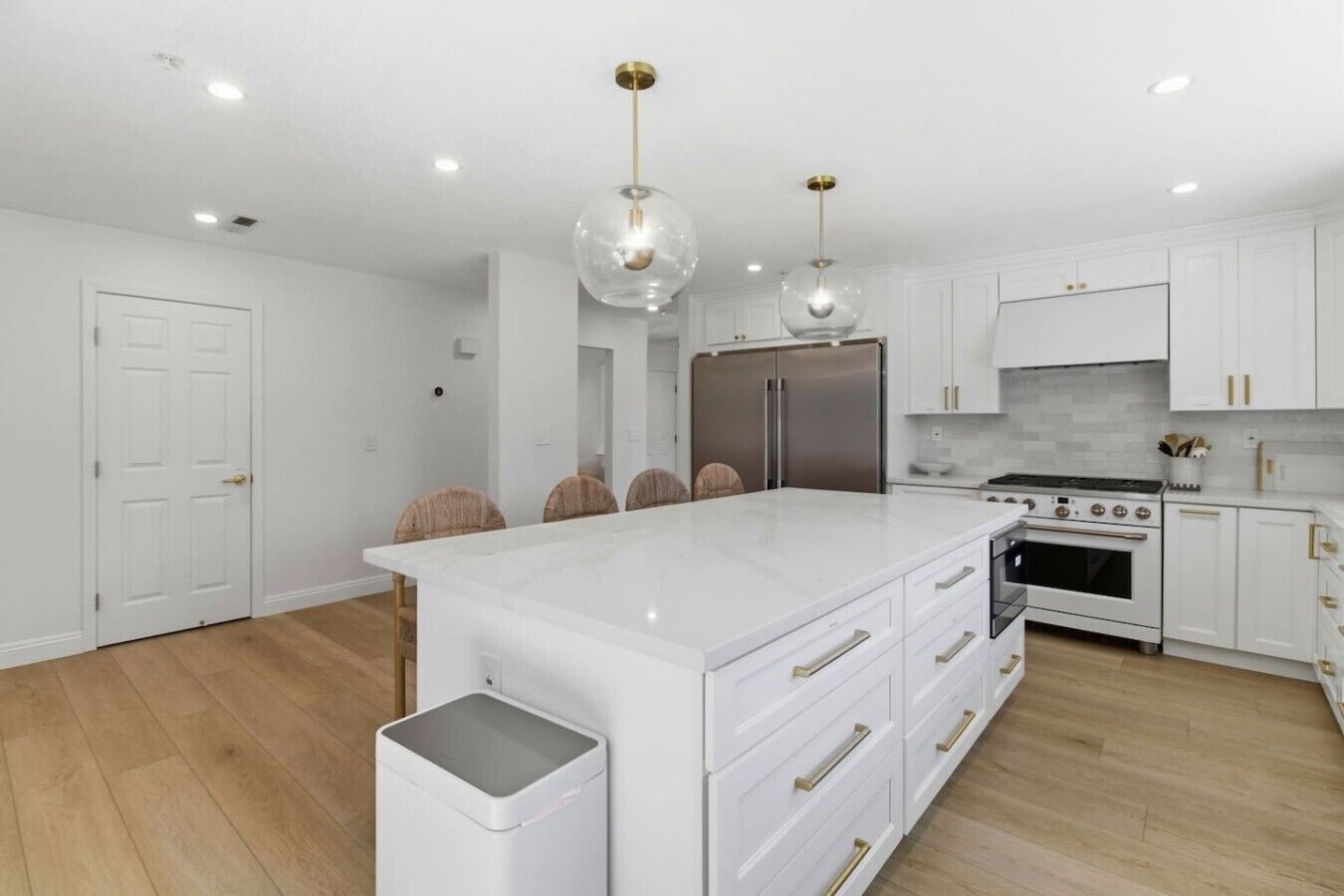 A modern kitchen with white cabinetry, a central island, stainless steel appliances, and pendant lighting.