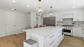 A modern kitchen with white cabinetry, a central island, stainless steel appliances, and pendant lighting.