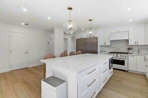 A modern kitchen with white cabinetry, a central island, stainless steel appliances, and pendant lighting. - Chic 3BR w/ Private Fenced Backyard Oasis (Foster City)