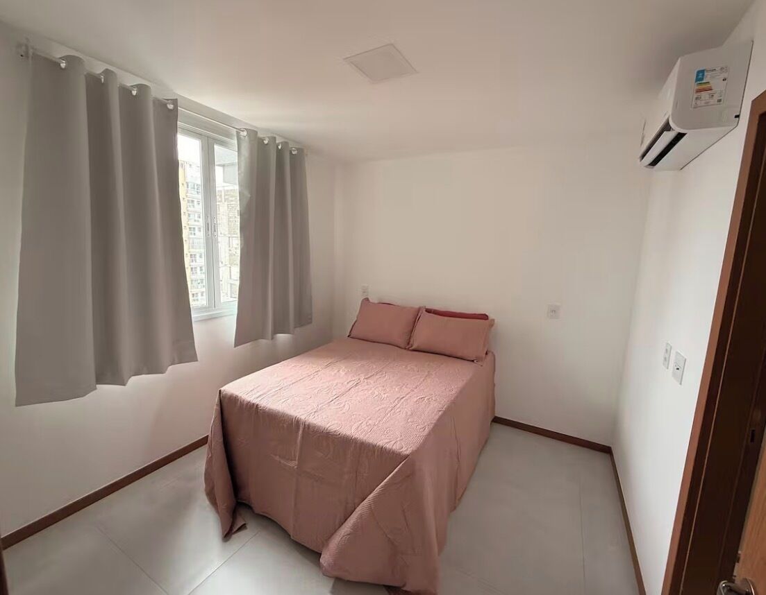 Un dormitorio con cama, cortinas, unidad de aire acondicionado y ventana.