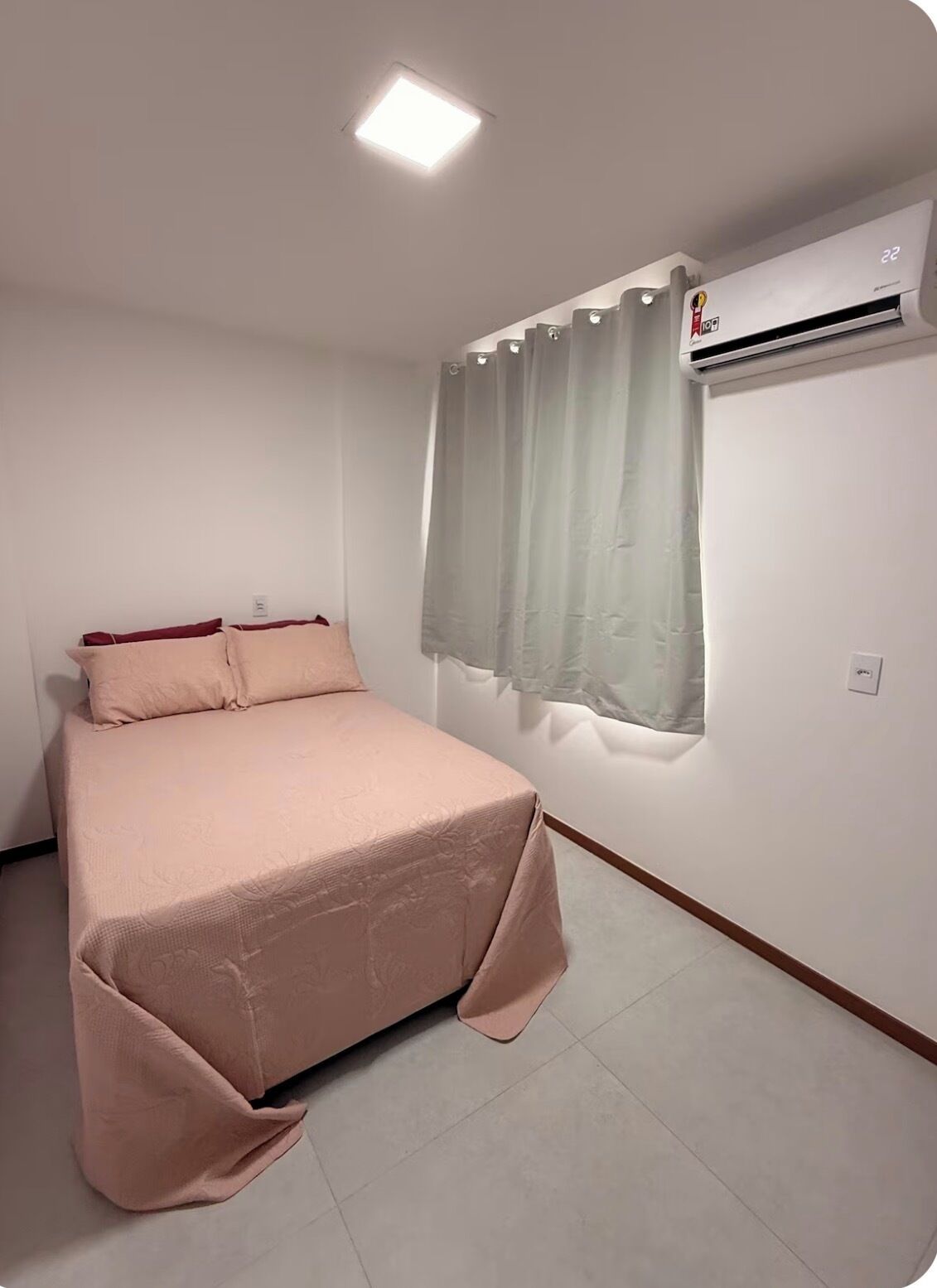 Un dormitorio con cama, ventana con cortinas, aire acondicionado y una lámpara en el techo.