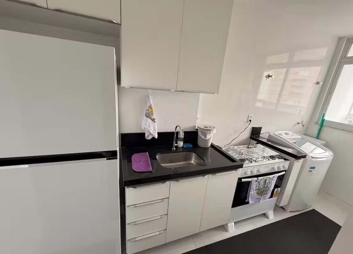 Una cocina moderna con armarios blancos, una encimera negra, un lavamanos, una estufa y un cubo de basura.