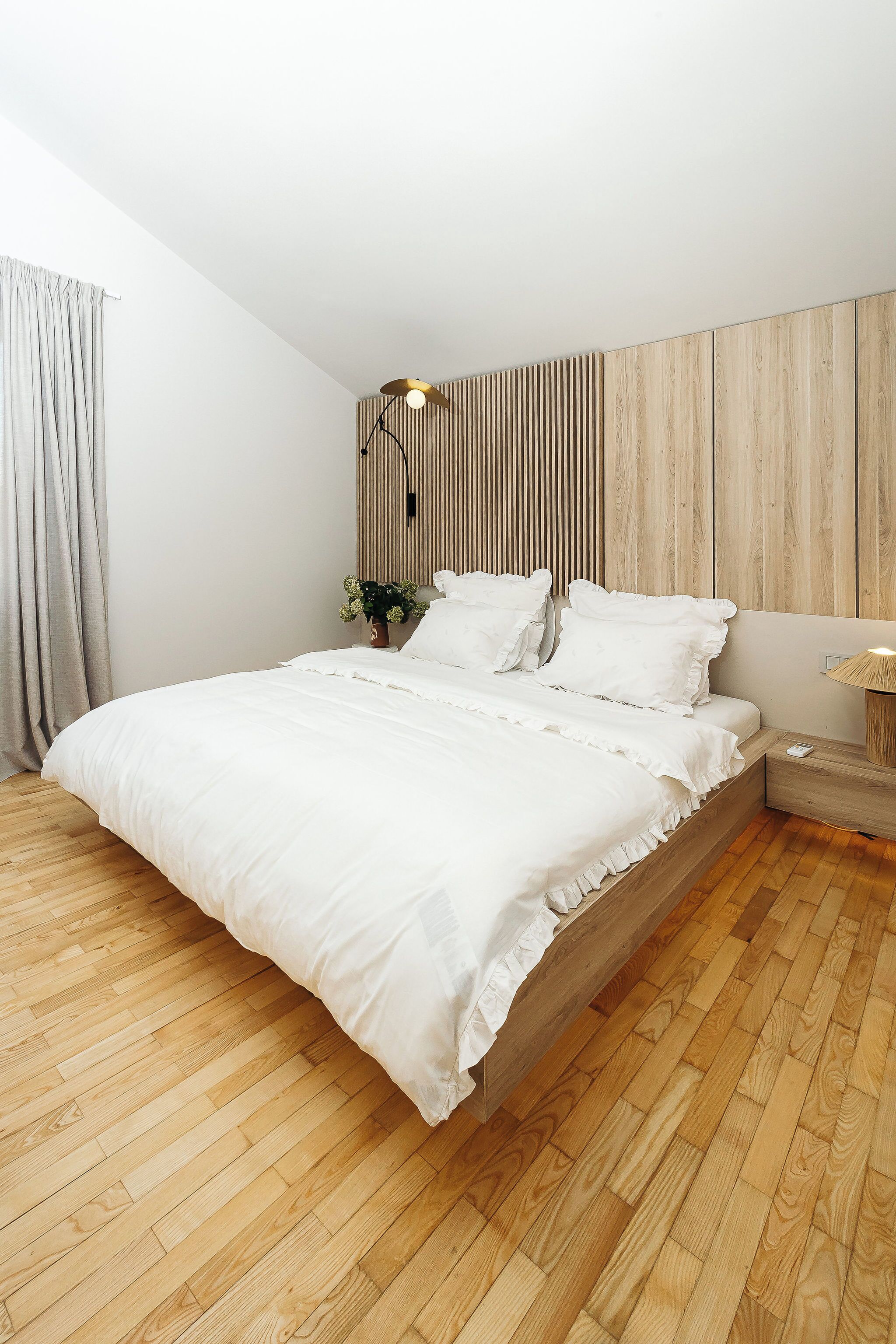Ein modernes Schlafzimmer mit einem großen Bett, Holzboden, einer Wandleuchte und einem Nachttisch mit Lampe.
