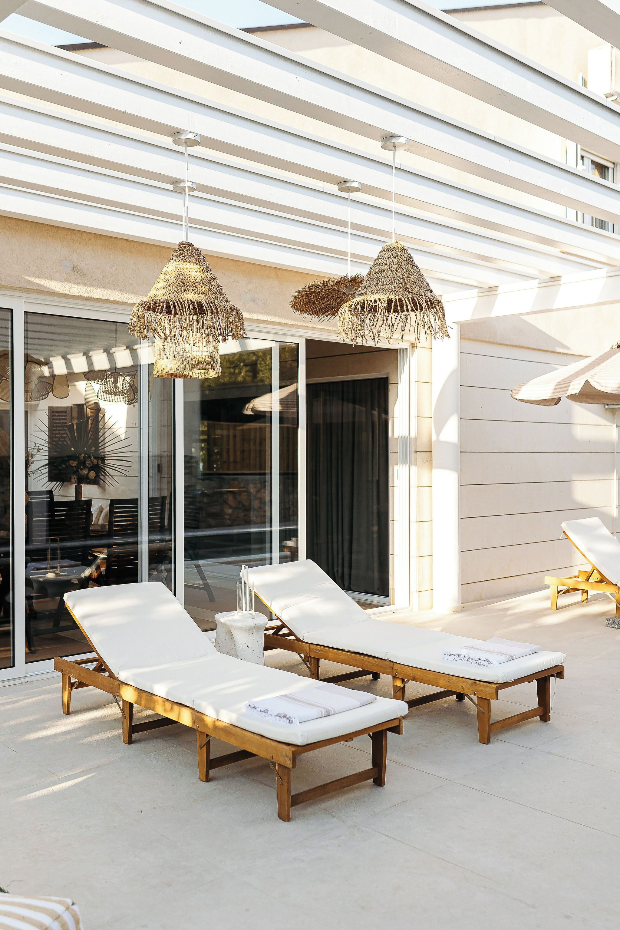 Een zonnig terras met twee houten lounge fauteuils en twee gevlochten hanglampen.