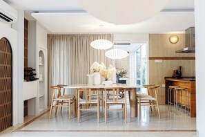 A modern dining area with a wooden table and chairs, a chandelier, and a view of the kitchen. - Luxurious Villa Ksenia with Pool Murter (Murter)