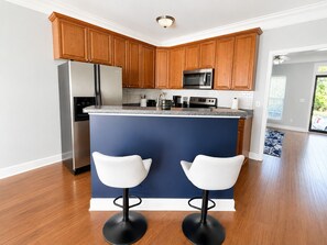 Une cuisine moderne avec des meubles en bois, des appareils en acier inoxydable et un îlot central bleu agrémenté de deux tabourets de bar blancs.