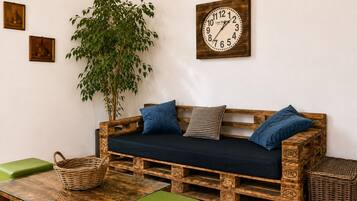 Un sofá de madera rústico con cojines, un reloj de pared y una planta verde en una habitación con un diseño sencillo y limpio.
