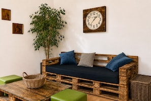 A rustic wooden sofa with cushions, a wall clock, and a green plant in a room with a simple, clean design. - Elegant 2BR Near Belvedere & Rennweg (Vienna)