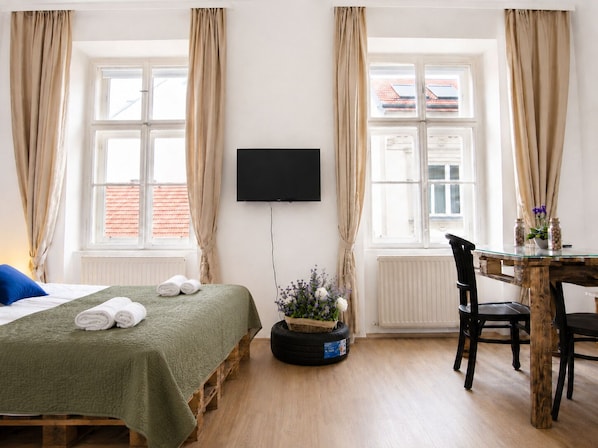 A room with a bed, a table, a chair, a television, and a window with curtains. - Elegant 2BR Near Belvedere & Rennweg (Vienna)