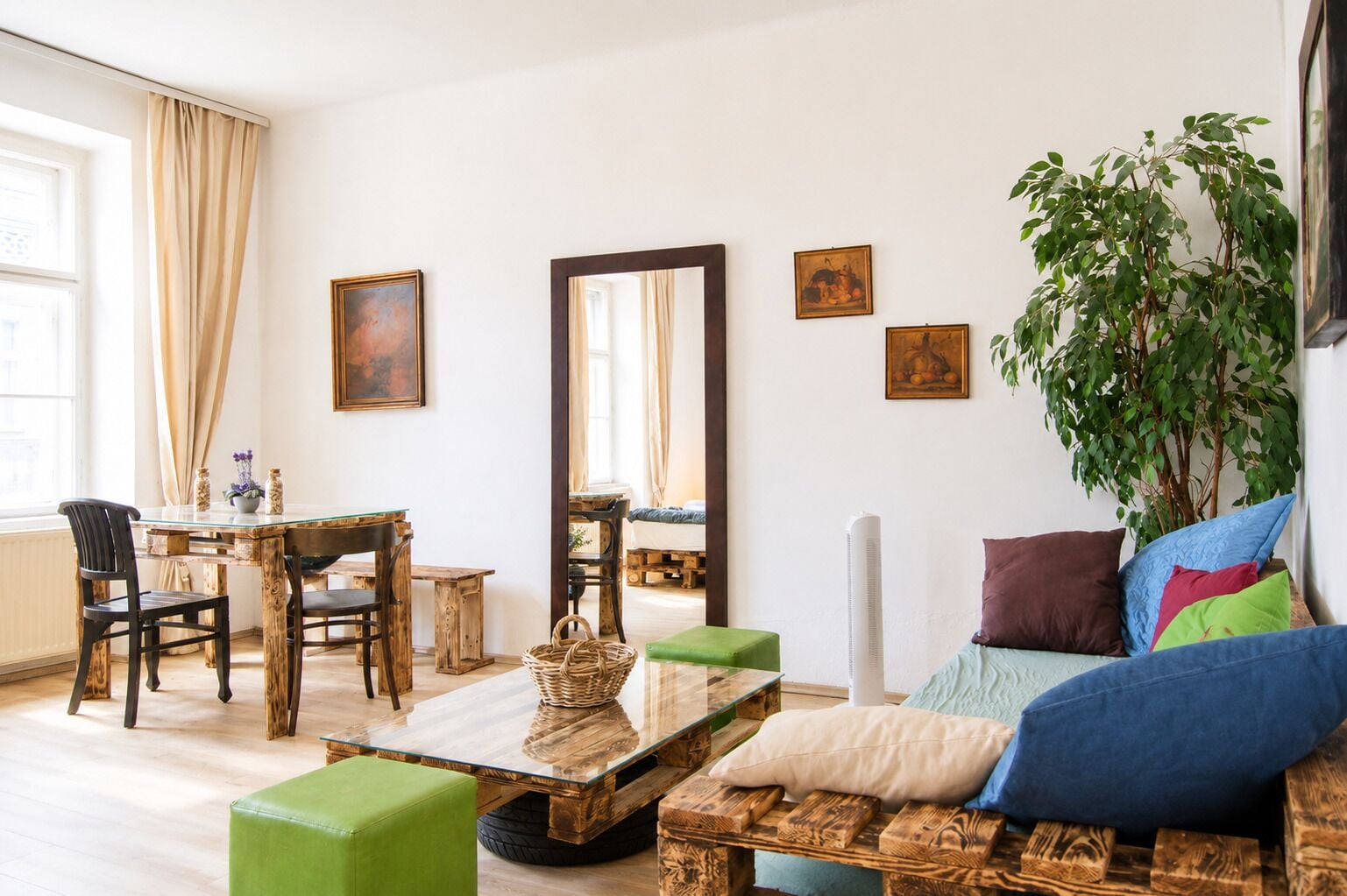 Una sala de estar con una mesa de comedor de madera, sillas, un sofá con cojines, un espejo grande y una planta en maceta.