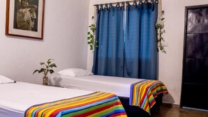 A hotel room with two beds, a large window with blue curtains, a framed picture on the wall, and a potted plant. - HOSTAL VILLA GUADUA TAYRONA (Santa Marta)