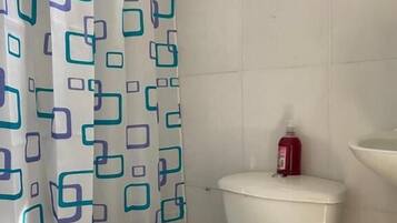 Une salle de bain avec des toilettes, un rideau de douche et une bouteille rouge posée sur le réservoir des toilettes.