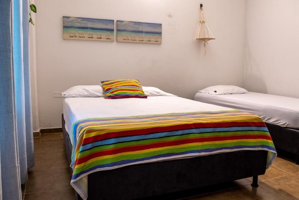 Un dormitorio con dos camas, una manta a rayas coloridas, almohadas blancas y una lámpara colgante.