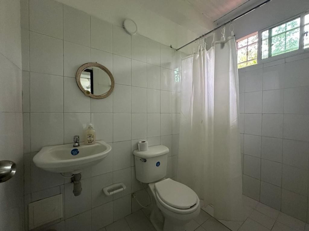 Casa de banho com lavatório branco, sanita e cortina de chuveiro.