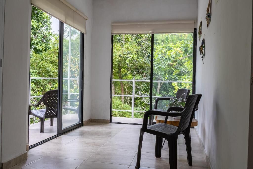 Een kamer met een schuifglazen deur naar een balkon, een eettafel met stoelen, en uitzicht op groen.