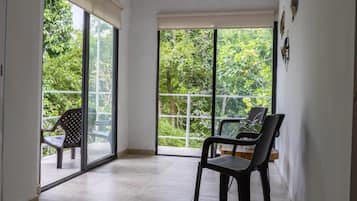 Een kamer met een schuifglazen deur naar een balkon, een eettafel met stoelen, en uitzicht op groen.