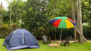 Una carpa montada en un césped, con un paraguas colorido y dos sillas.