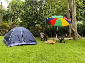 Une tente installée sur une pelouse, avec un parasol coloré et deux chaises.