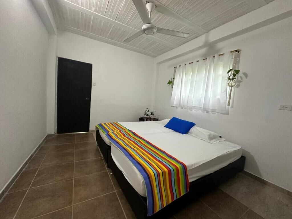 A bedroom with a bed, a ceiling fan, a window with curtains, and a door.