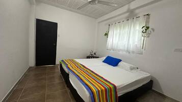 A bedroom with a bed, a ceiling fan, a window with curtains, and a door.