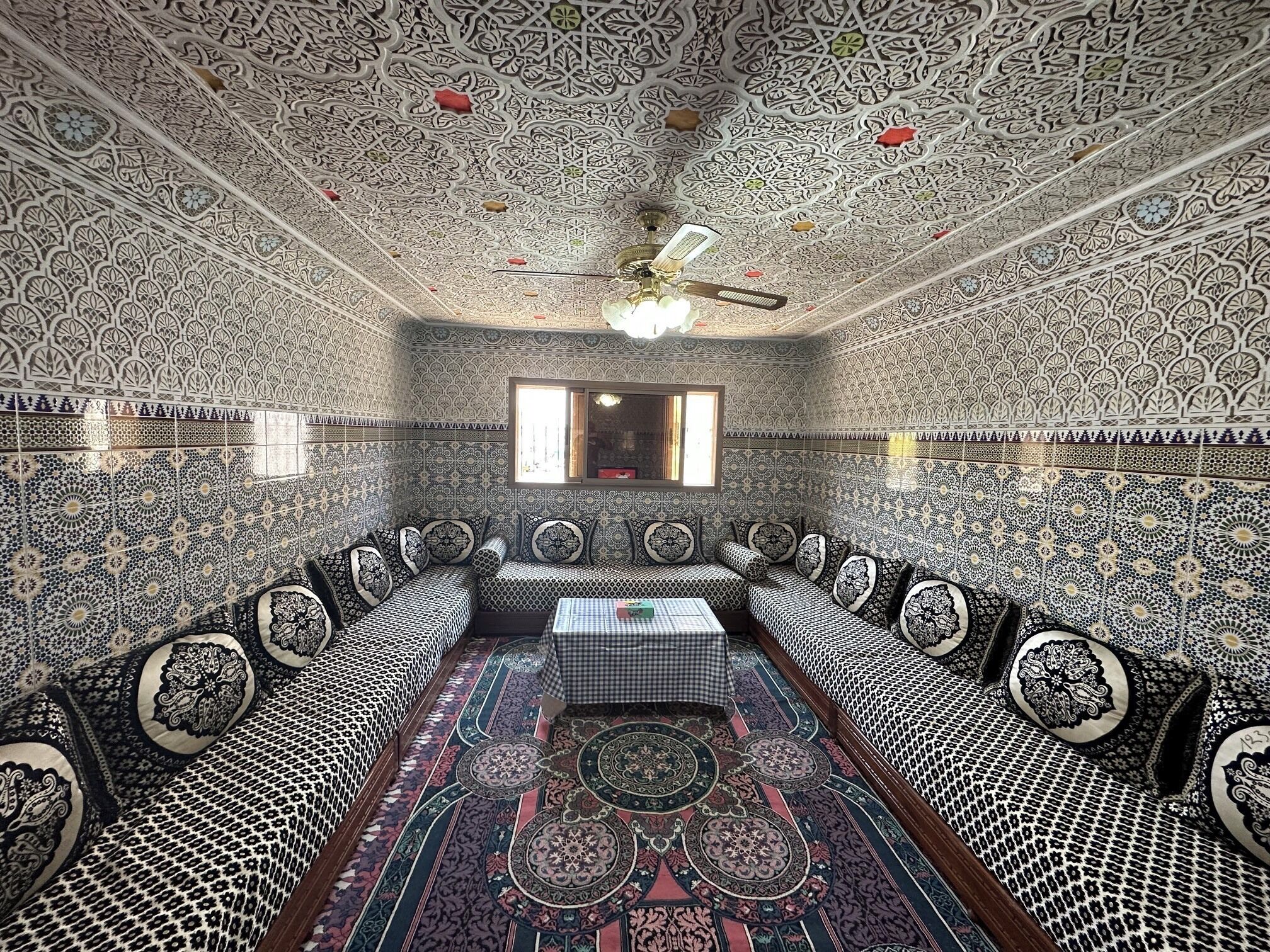 Een kamer met gedetailleerde behangpanelen en een zithoek met een geruit tafelkleed.