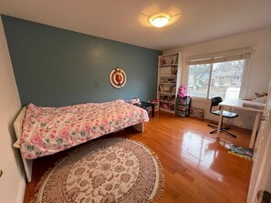 Ein Schlafzimmer mit Bett, Schreibtisch, Bücherregal und Fenster.